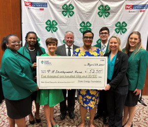 A group stands together with a check in front of a 4-H Backdrop.